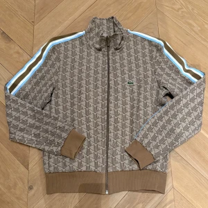 Lacoste track jacket - Säljer denna riktigt feta Lacoste Monogram Track Jacket. Tröjan är väldigt eftertraktad och slutsåld. Tröjan är beige med ljusblåa detaljer på armarna. Den är i storlek S, Fransk 3. Tröjan är i väldigt bra skick eftersom att den är bara använd ett fåtal gånger. Skriv vid fundering. Pris kan diskuteras