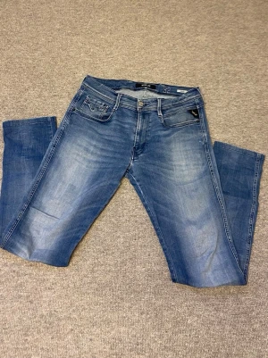 Blå jeans från Replay herrmodell - Snygga blå jeans från Replay med klassisk femficksdesign och diskreta slitningar framtill. Jeansen har raka ben och detaljerade bakfickor med broderi. Tillverkade i bomull med en skön passform, perfekta för en avslappnad stil. Skriv om ni har frågor!