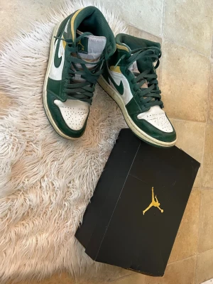 Air Jordan 1 Mid grön/vit/gul - Säljer ett par Air Jordan 1 Mid sneakers i grönt, vitt och gult. Klassisk hög siluett med gröna läderpaneler, vit tåbox och sidor samt gula detaljer vid ankeln. Ikonisk Swoosh på sidan och Air Jordan-logga på ankeln. Kommer med originalkartong. Ej fast pris går att diskutera.
