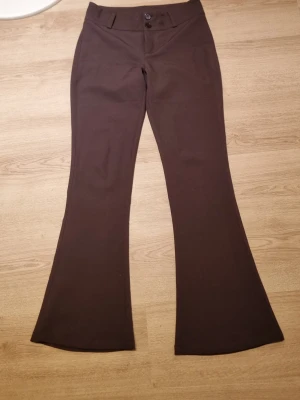 Bruna utsvängda kostymbyxor - Säljer ett par bruna kostymbyxor med utsvängda ben. Byxorna har två knappar fram, fickor bak med knapp samt bälteshällor. Perfekta för en trendig och stilren look.