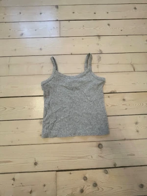 Grå ribbad linnetopp - En enkel och stilren grå linnetopp med smala axelband och ribbad struktur. Perfekt att matcha med jeans eller kjol för en avslappnad look.