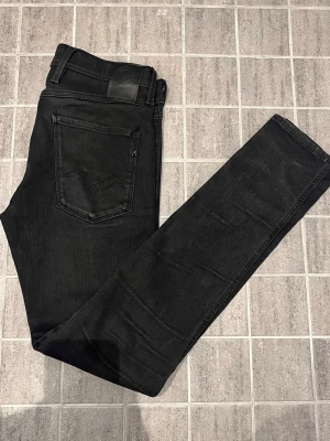Svarta jeans från Replay - Säljer ett par svarta jeans från Replay med klassisk femficksdesign och raka ben. Jeansen har en snygg svart läderpatch bak i midjan och Replay-logga vid bakfickan. Tillverkade i stretchig denim för skön passform.31:32