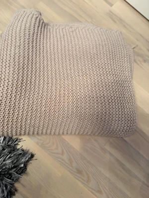Beige stickad filt storlek 150, 200 - Stor beige stickad filt i grovt garn med rektangulär form. Färgen är neutral och passar lätt in i olika inredningsstilar. Materialet känns mjukt och filten är perfekt att ha i soffan eller på sängen för extra mysfaktor.