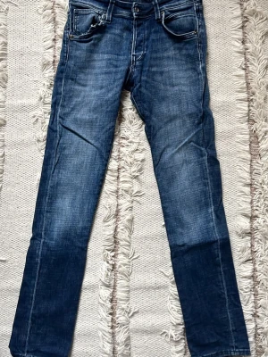 Mörkblå slim fit jeans - Snygga mörkblå slim fit jeans med klassisk femficksdesign och lätt slitna detaljer. Jeansen har normal midja och raka ben, perfekta till en avslappnad stil. Tillverkade i denim med stretch för extra komfort.
