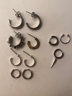 Örhängen - Säljer ett set med flera olika örhängen i både silver- och guldfärg. Blandningen inkluderar hoops, örhängen med nitar, en med spetsig detalj och några med små kulor. Materialet ser ut att vara metall. Perfekt för dig som gillar att mixa stilar och former. Ett par 20kr/st. 1 örhänge 10kr/st🤍alla 11 örhängen 100kr!