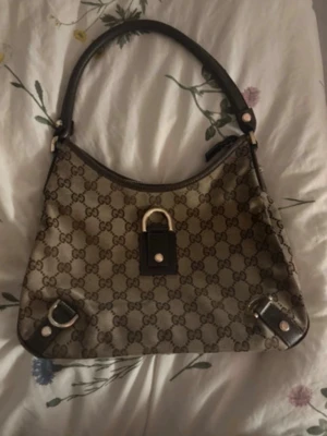 Gucci brun monogram handväska - Snygg handväska från Gucci, väskan är i väldigt fint skick och kan bäras på axeln. Väskan är självklart äkta. Priset kan diskuteras vid snabb affär, hör av er vid frågor eller om ni vill ha fler bilder💓