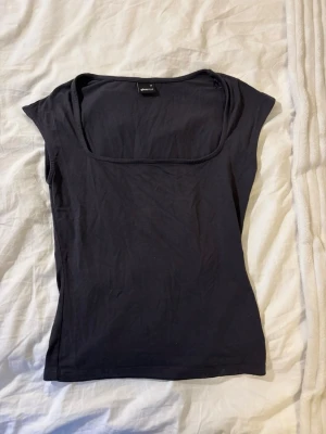 Mörk grå topp från Gina Tricot - En grå, tight topp från Gina Tricot med fyrkantig ringning och korta ärmar. Säljer för att den inte kommer till användning längre💗💗