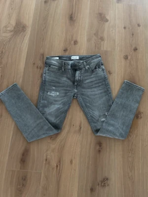 Ljusgråa Jeans från JJ - Säljer ett par gråa jeans från Jack & Jones med lite slitningar 