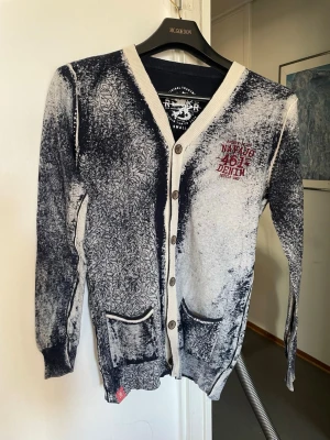 Svartvit kofta  - Unik svartvit kofta med kontrastfärgade kanter och knappar framtill. Tryckt text och logga på bröstet samt coolt mönster och två fickor fram. Perfekt för dig som gillar streetwear och statement-plagg.