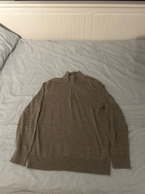 Beige stickad halvziptröja  - Säljer en beige stickad tröja från H&M med halvzip och hög krage. Tröjan har långa ärmar och ribbade muddar vid ärmslut och nederkant. Perfekt för lager på lager och enkel att matcha med olika outfits. Har ett litet hål på ryggen 
