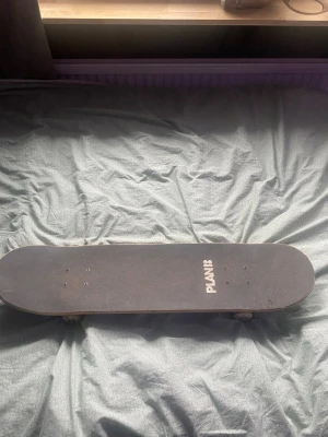 Plan B skateboard med färgglad design - Säljer en skateboard från Plan B med svart griptape på ovansidan och en färgglad tie-dye design undertill. Brädan har vita hjul och silverfärgade trucks. Perfekt för dig som vill sticka ut i skateparken.