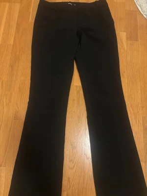 Svarta kostymbyxor från BikBok - Säljer lågmidjanse  svarta kostymbyxor från BikBok i rak modell med lätt utsvängda ben.Knappen vid midjan har lossnat men funkar fortfarande perfekt 