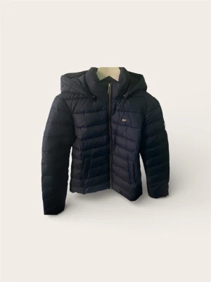 Tommy Hilfiger Dunjacka (XS) – Helt ny/Oanvänd - Säljer en stilren och varm dunjacka från Tommy Hilfiger i marinblått. Jackan är helt oanvänd då returdatumet missades.  Klassisk modell med huva och den ikoniska lilla loggan på bröstet. Perfekt vår/höst/vinterjacka som håller värmen bra utan att vara klumpig.  Skick: Nyskick! Aldrig använd, endast provad.  Storlek: XS.  Nypris 2 500 kr.