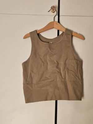 Beige ribbad crop top från H&M - Säljer en beige ribbad crop top från H&M. Materialet är stretchigt och mjukt, perfekt för träning eller som ett basplagg. Nästan aldrig använd, men tvättad för försäljning.