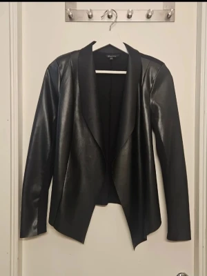 Svart skinnjacka / kavaj i nyskick  - Snygg svart skinnjacka från Only med öppen front och lång ärm. Jackan har en modern, lite längre passform och breda slag som ger en cool look. Perfekt för att lyfta vilken outfit som helst med en edgy touch. Endast provad så i nyskick.