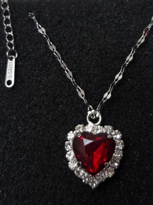 ❤️ OTROLIGT RÖTT HJÄRTHALSBAND – ROSTFRITT STÅL ❤️ - Säljer detta helt magiska halsband med ett djupt rubinrött hjärta omringat av gnistrande stenar. Ger en lyxig vintage-känsla och påminner om det ikoniska ”Heart of the Ocean”, fast i en passionerad röd färg! ✨ Perfekt för att piffa upp en enkel outfit eller som en speciell gåva. Detaljer: Material: Högkvalitativt rostfritt stål (tål vatten, missfärgas inte och är allergivänligt). 💧 Skick: Helt nytt och oanvänt! 🌟 Stil: Vintage / Romantic / Y2K / Coquette aesthetic.