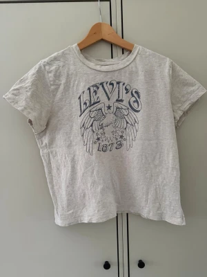 Levi's grå t-shirt med tryck - Snygg grå t-shirt från Levi's med coolt örntryck och texten 'Levi's 1873' på bröstet. Klassisk rund hals och korta ärmar. Perfekt för en avslappnad stil.