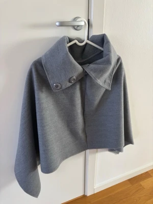 Grå cape/poncho  - Snygg grå cape/ poncho i fint skick! Modellen är kortare och har en stilren, minimalistisk design. Materialet känns mjukt och följsamt.