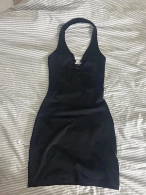 Svart halterneck kortklänning - Snygg svart kortklänning med halterneck och djup v-ringning. Klänningen har en figurnära passform och är tillverkad i ett slätt material som ger en stilren look. 