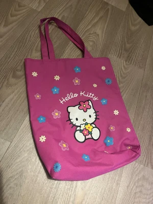 Hello Kitty rosa totebag  - Söt rosa totebag/tygväska med Hello Kitty-tryck och färgglada blommor på framsidan.