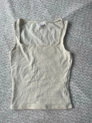 Beige linnetopp från Gina Tricot - Säljer en stilren gul linnetopp från Gina Tricot, Elevated Basics. Toppen har en fyrkantig urringning och är ärmlös, perfekt för lager på lager eller sommarens varma dagar. Enkel och clean design som passar till allt.