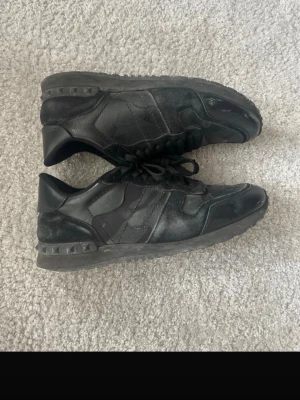 Svarta sneakers från Valentino - Säljer ett par helsvarta sneakers från Valentino med coola nitar på sulan. Skorna har en mix av mocka och läderdetaljer, samt svarta skosnören. Snygg och stilren design som passar till det mesta.