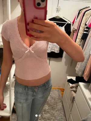 Ljusrosa ribbad omlottopp - Söt ljusrosa topp med ribbad struktur och omlottdesign. Toppen har korta ärmar, v-ringning och en liten rosett framtill. Perfekt för dig som gillar en feminin och trendig stil. Nypris-399kr.