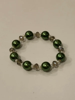 Grönt pärlarmband  - Handgjort armband med stora gröna pärlor, små vita pärlor och facetterade genomskinliga glaspärlor. Armbandet har en elastisk tråd som gör det enkelt att ta på och av. 