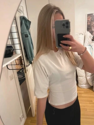 Vit croppad topp med knyt i ryggen - Trendig vit croppad topp med korta ärmar och snygg öppen rygg som knyts med ett brett band. Perfekt för dig som vill ha en stilren men ändå unik look. Toppens material känns mjukt och lätt mot huden.