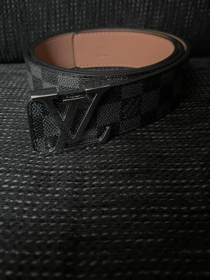 L-v Svart rutigt bälte - Säljer ett helt nytt riktigt snyggt svart L-v bälte med silver logga.