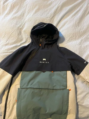 Montec anorakjacka Dune W - Snygg anorakjacka från Montec i färgblockad design med svart, grågrön och vit. Stor ficka framtill, dragkedja vid halsen och huva. Orange detaljer på dragkedjor och knappar. Perfekt för dig som gillar streetwear och funktionell stil. Nypris 2000kr, endast använd en gång. Mycket bra skick!