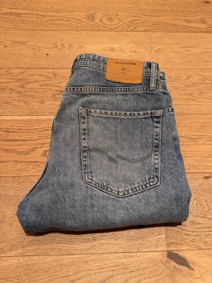 Blå raka jeans från Jack & Jones - Klassiska blå jeans från Jack & Jones i rak modell. Jeansen har en bakficka med diskret söm och en brun läderpatch med logga i midjan. Tillverkade i slitstarkt denimtyg som ger en tidlös look. Modell Loose / Chris. Stl 30/30.
