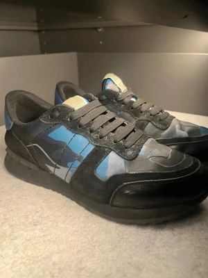 Rockrunners - Snygga sneakers från Valentino med blått och svart kamouflagemönster.kom privat för fler bilder Skorna har svarta snören, svart sula och detaljer i mocka och läder. Perfekta för dig som vill sticka ut med en cool och modern stil.