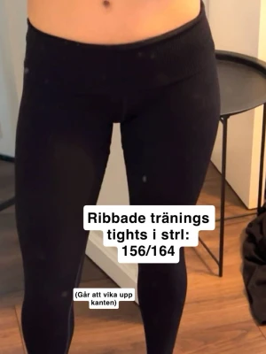 Ribbade svarta träningstights - Säljer ett par ribbade svarta träningstights med hög midja som går att vika ner. Tightsen har en tight passform och är perfekta för träning eller chill. Materialet är stretchigt och följsamt för bästa komfort.
