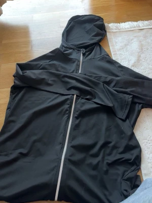 Svart hoodie med dragkedja - Säljer en svart hoodie med hel dragkedja framtill och huva. Hoodien har en enkel och stilren design, perfekt för en avslappnad look. Materialet känns mjukt och bekvämt mot huden. Passar bra till jeans eller träningsbyxor.