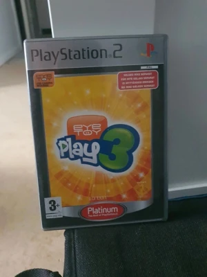 EyeToy Play 3 till PS2 - EyeToy Play 3 till PlayStation 2 är ett partyspel där du använder EyeToy-kameran för att spela över 50 olika minispel. Omslaget är färgglatt i gult och orange med stora logotyper. Spelet är i DVD-fodral och kräver EyeToy-kamera för att fungera.