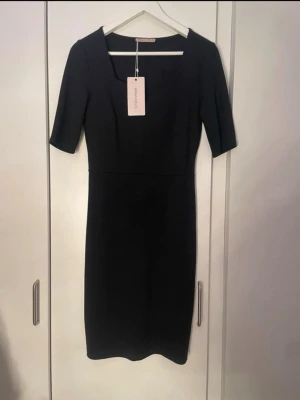 Svart kortklänning från Anna Field - Stilren svart kortklänning från Anna Field med fyrkantig ringning och halvlånga ärmar. Klänningen har en figurnära passform och är tillverkad i ett mjukt, stretchigt material som ger en bekväm känsla. Perfekt för dig som gillar enkel och klassisk stil.