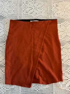 Rostbrun omlottkjol i bomull - Kort och tajt omlottkjol i en snygg rostbrun/ orange färg. Kjolen har en enkel och stilren design med omlottdetalj framtill och är gjord i mjukt bomullsmaterial. Säljer då den inte används🤎🧡