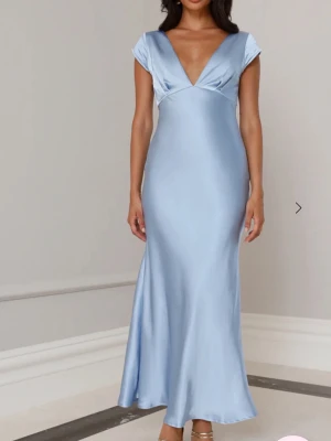 Ljusblå långklänning i satin - Elegant ljusblå långklänning i glansigt satinmaterial med djup v-ringning och korta ärmar. Perfekt till en bal eller ett bröllop! Aldrig använd! Nypris 1300kr🥰