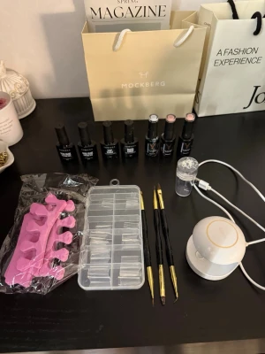 Nagelkit med UV-lampa och geléer - Komplett nagelkit med vit UV-lampa, flera gelélack i olika färger, penslar med svart och guld handtag, rosa tåseparerare, plasttips i ask och stämpel. Perfekt för att fixa snygga naglar hemma och skapa egna designer.