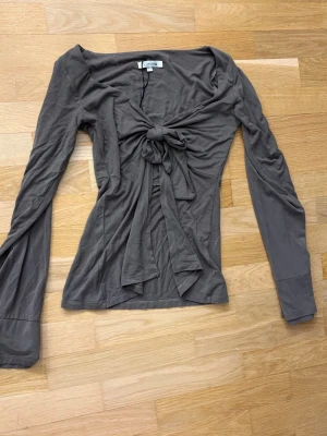 Brun långärmad topp med knyt - Snygg brun långärmad topp från Desing by dimed stor knytning framtill. Toppen har en figurnära passform och är tillverkad i mjuk bomull, perfekt för att lyfta vilken outfit som helst.