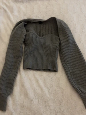 Grå ribbstickad croppad tröja -  grå stickad tröja med croppad passform och markerad sweetheart-urringning. Tröjan har långa ärmar och är ribbstickad för en snygg struktur. Perfekt för lager-på-lager och passar till både jeans och kjol.