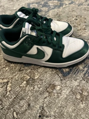 Nike low dunk green satin - Använd max 5 gånger. Det finns veck på tån och loggan på innersulan är sliten Annars är dom i gott skick, inga fläckar, hål eller större skador. Bud är välkomna! 😊