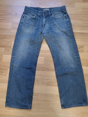 Blå raka jeans - Klassiska blå jeans från Lee med rak passform och fem fickor. Jeansen har en avslappnad look med diskreta slitningar och Lee-logga på bakfickan. Tillverkade i denim med en tidlös tvätt som passar till det mesta.