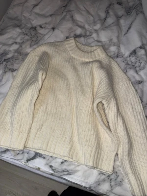Krämvit stickad tröja  - Mysig krämvit stickad tröja med grov ribbstickning och rund halsringning. Tröjan har en avslappnad passform, långa ärmar och breda muddar. Perfekt för lager på lager och enkel att matcha med jeans eller kjol.