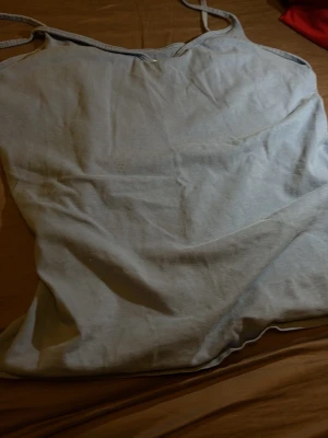 Blå enkel linnetopp - Säljer en blå linnetopp med tunna axelband. Toppen har en enkel och clean design, perfekt att matcha med olika outfits. Materialet känns mjukt och lätt, vilket gör den skön att bära under varma dagar.