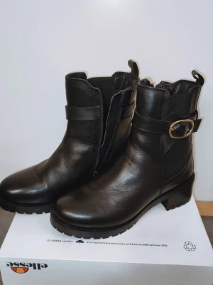 Svarta stövletter i skinn från Dasia - Snygga svarta stövletter från Dasia i äkta skinn med robust sula och låg klack. Dekorativt spänne i metall på sidan och dragkedja på insidan för enkel på- och avtagning. Klassisk och stilren design som passar till många outfits. Ej använda. 