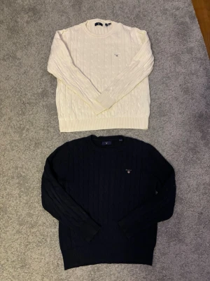 Stickade tröjor från GANT, vit & marinblå - Två klassiska stickade tröjor från GANT, en i offwhite och en i marinblått. Båda har kabelstickat mönster, Det går också att köpa st! Om du vill köpa en så är det bara att diskutera pris. Storlek på blåa är 146/152. Vita är 158/164,  