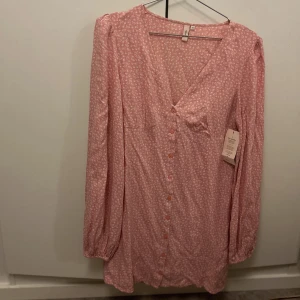 Rosa blommig kortklänning  - Rosa kortklänning från Nelly med små vita blommor. Aldrig använd endast testad. Storlek 38