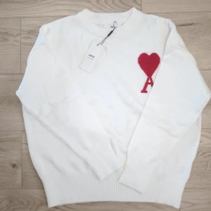 Vit kofta från Ami Paris - Vit stickad kofta från Ami Paris med rött broderat hjärta och bokstaven A.                       🐑Tillverkad i bommul och ull.                            📏Storlek: M, Overzised fit                                 ⭐Oanvänd med lapp